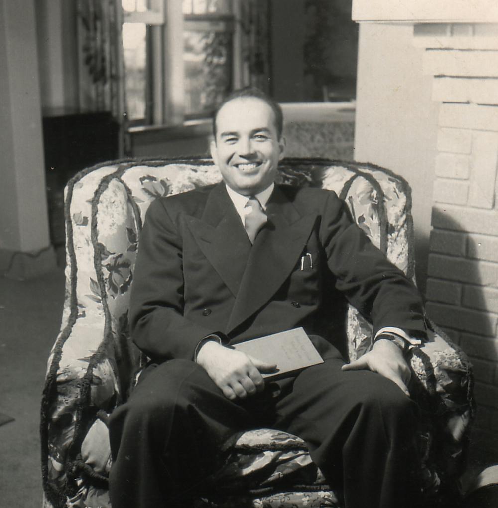 Stanley seated in an armchair smiling while holding a book