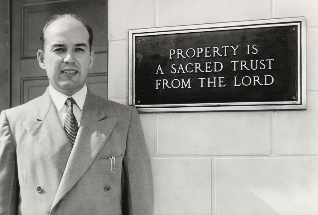 Stanley with a wall plaque: "Property is a Sacred Trust from The Lord"